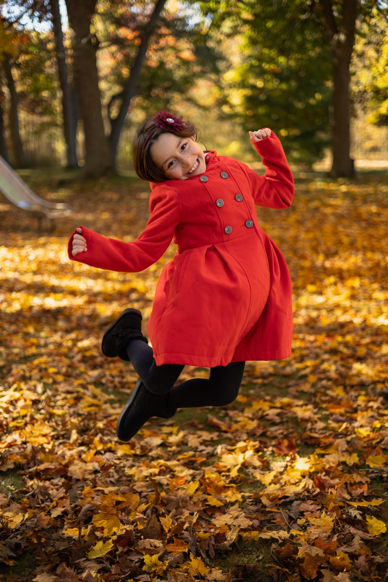 Child in a red coat moving through fallen autumn leaves