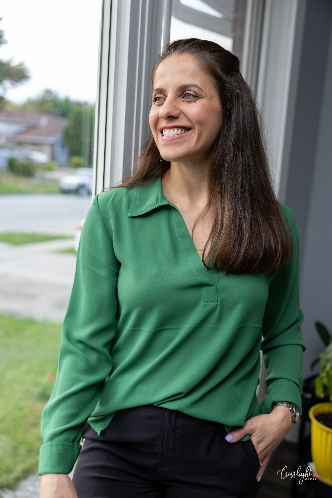 Woman in a green blouse smiling beside a window