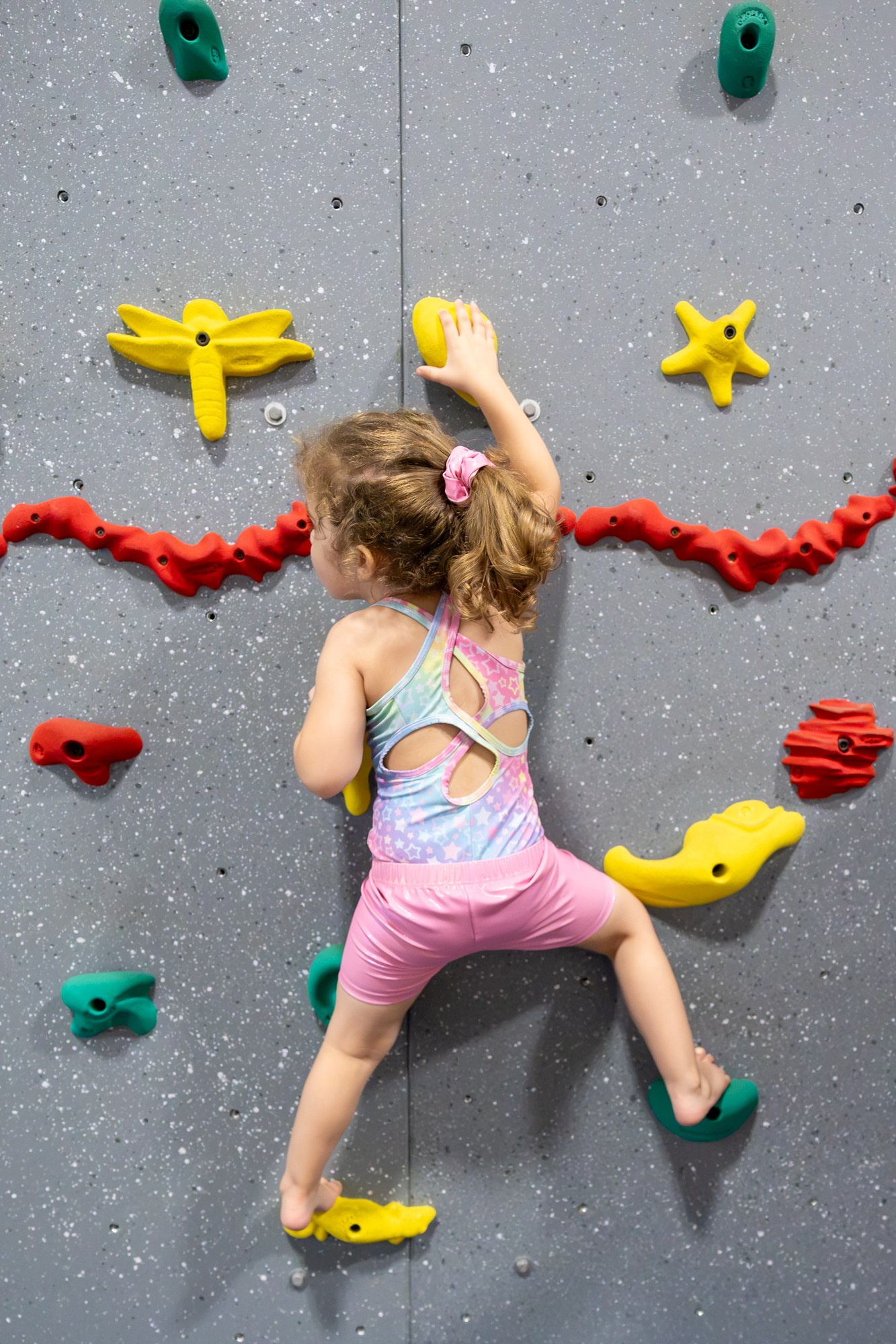 Child reaching for colourful climbing holds with hands and feet on the wall
