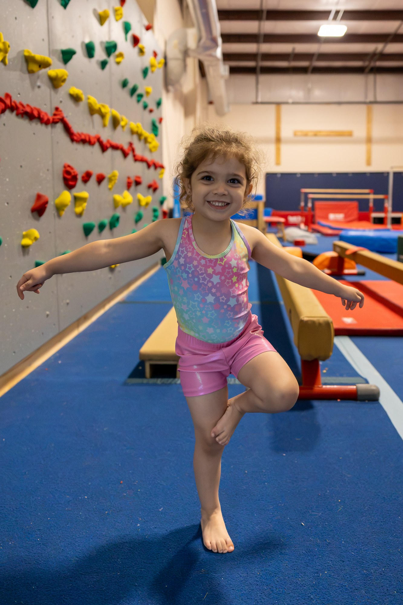 Gymnast balancing on one foot with arms outstretched beside a balance beam