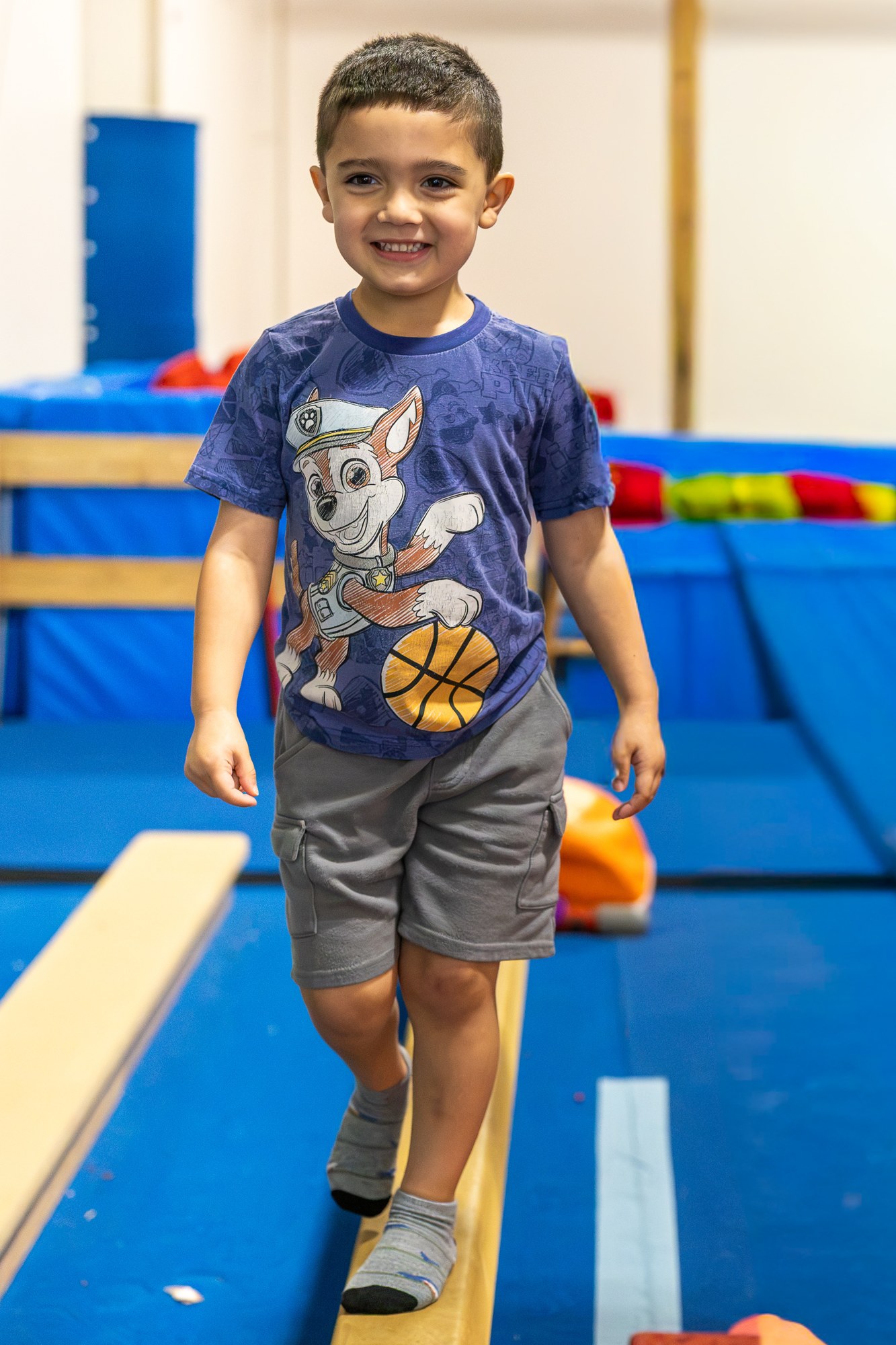 Smiling child walking along a low balance beam in a gymnastics space