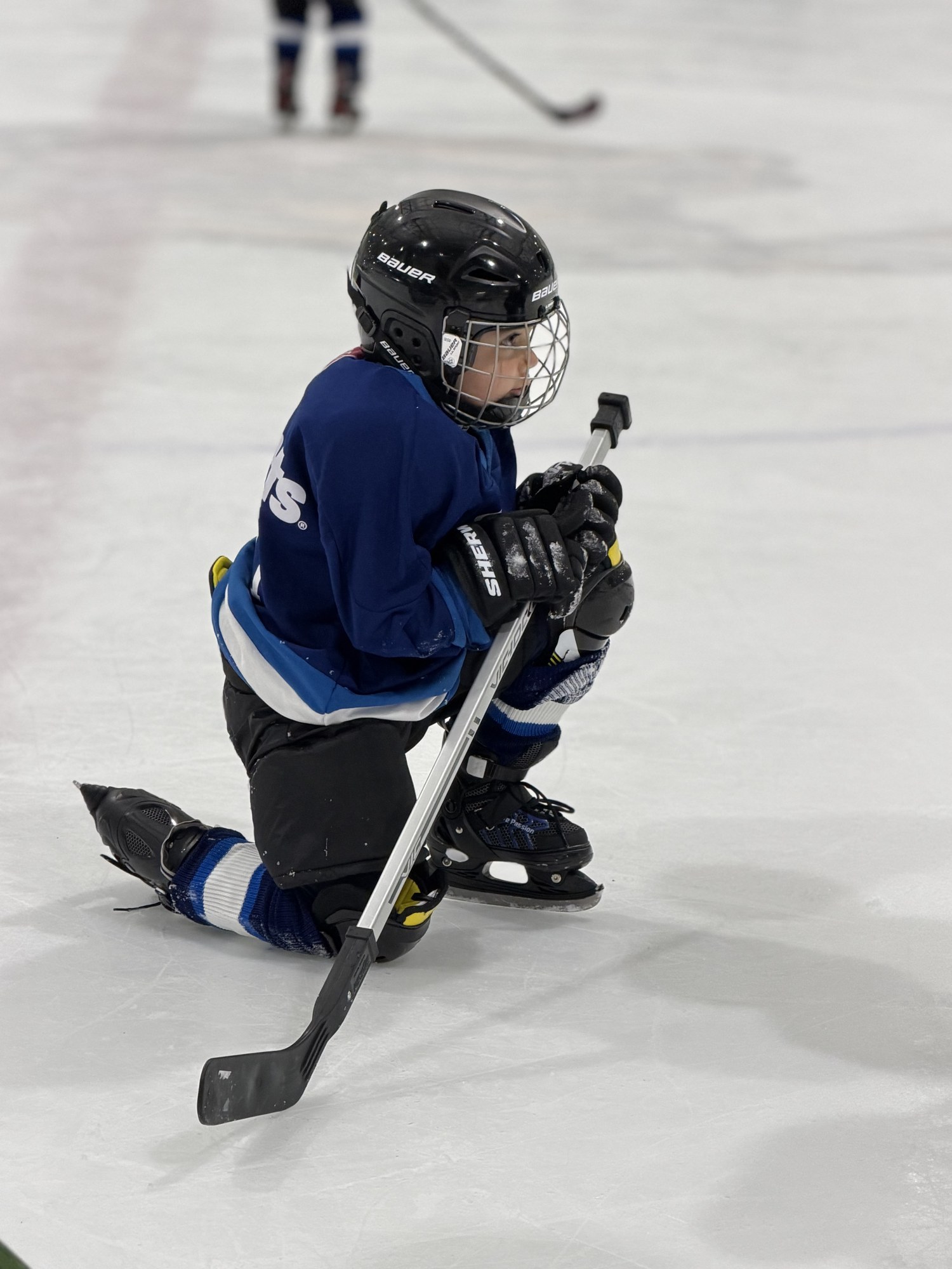 Hockey player kneeling on the ice with helmet, gloves, skates, and stick
